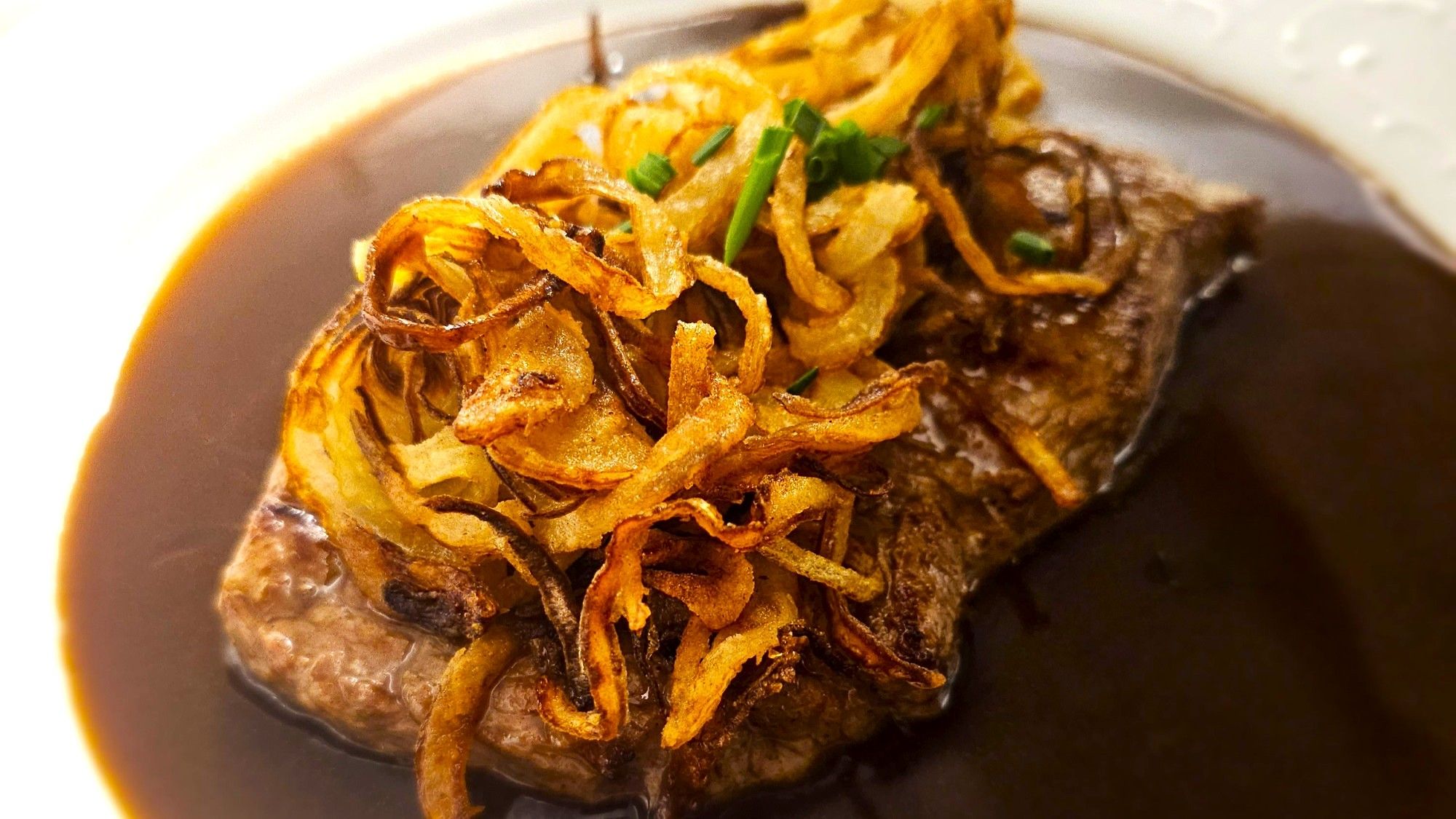 Ein Teller mit einem Steak und Zwiebeln darauf.